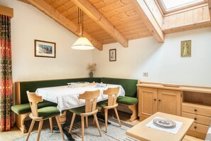 A dining area with a wooden table, green cushioned bench, and a high wooden ceiling with a skylight.