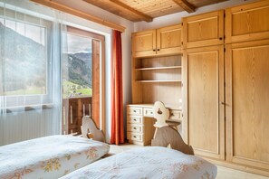 A bedroom with two beds, wooden wardrobe, and a view of the mountains.