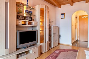 Een moderne woonkamer met een flatscreen televisie, houten kastjes en een glazen plank met decoratieve objecten.