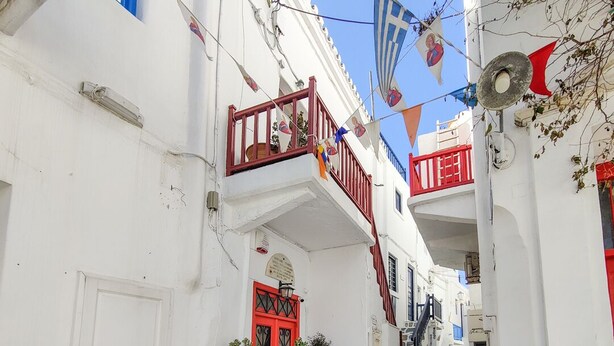 Une rue étroite bordée d’immeubles blancs, de portes rouges et de balcons.