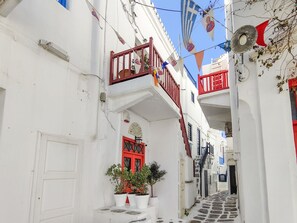 A narrow street with white buildings, red doors, and balconies.