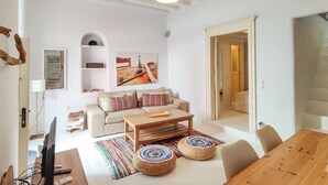 Un vaste espace de vie comprenant une table basse en bois, un canapé et une table à manger. On y trouve également un téléviseur posé sur un meuble, une bibliothèque et un tableau accroché au mur.