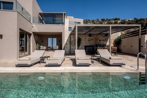 A modern outdoor pool area with lounge chairs, a stone wall, and a barbecue area.