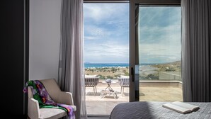 A bedroom with a large sliding glass door leading to a balcony with a view of the sea and landscape.