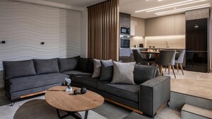 A modern living room with a sectional sofa, a wooden coffee table, and a kitchen area with a dining table and chairs.