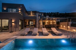 A modern house with a swimming pool, outdoor seating, and a stone wall.