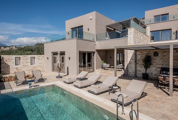 A modern villa with a pool, outdoor seating, and a stone facade.
