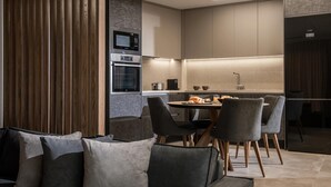 A modern kitchen with built-in appliances, a dining area with grey upholstered chairs, and a wooden accent wall.