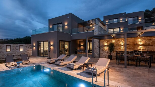 A modern villa with a swimming pool, outdoor seating, and a stone facade.