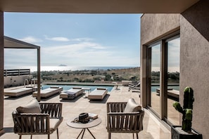 A balcony with a pool, outdoor seating, and a view of the sea and distant hills.