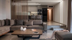 A modern living room with a sectional sofa, a coffee table with books and vases, and a kitchen in the background. - Villa Paradise 2 in Kalamaki (Faistos)