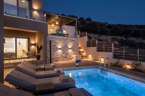 Ein moderner Poolbereich im Freien mit Liegestühlen, einem Grill und einer Steinmauer.