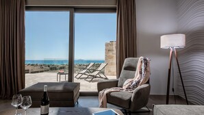A hotel room with a large window, a view of the sea, a lounge chair, a table with a bottle of wine, and a tablet. - Villa Paradise 2 in Kalamaki (Faistos)
