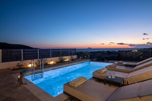 Ein Pool mit Wassersicht auf dem Dach, mit Liegestühlen und Blick auf den Sonnenuntergang.