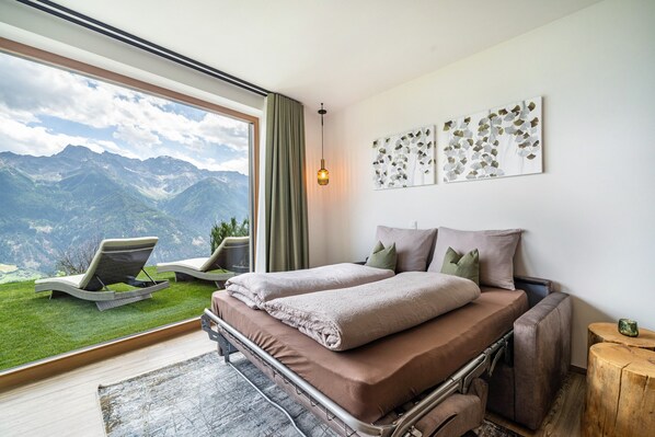 A bedroom with a large window, a bed, a chair, and a view of mountains.