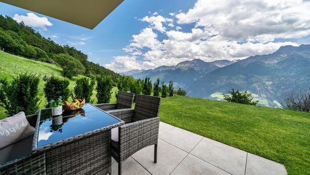 Une terrasse dotée de meubles en osier, d’une table en verre et offrant une vue sur les montagnes.