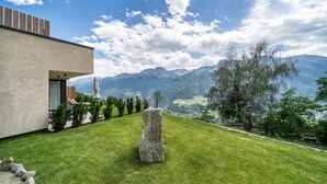 A modern building with a stone feature in the foreground, a patio area, and a mountainous landscape in the background. - Holiday Apartment "Paflur Lodges Abendrot" with Mountain View, Private Terrace & Wi-Fi (Lasa)