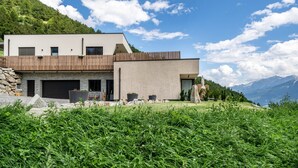 A modern house with a stone foundation, a flat roof, and a wooden deck. - Holiday Apartment "Paflur Lodges Abendrot" with Mountain View, Private Terrace & Wi-Fi (Lasa)
