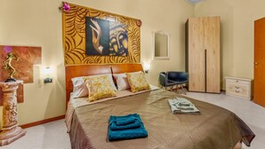 Quarto de hotel com cama, cabeceira com obra de arte, guarda-roupa, cadeira e mesa de cabeceira.