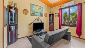 Sala de estar com sofá, televisão e estantes decorativas.