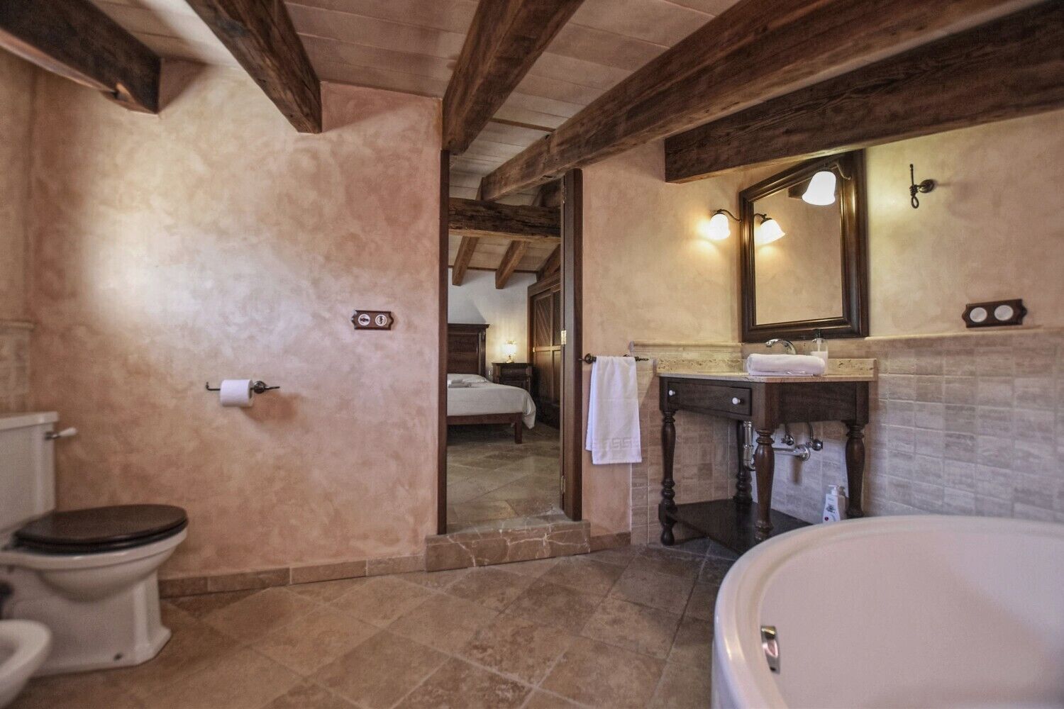 A bathroom with a toilet, sink, and bathtub, wooden beams on the ceiling, and a mirror above the sink.