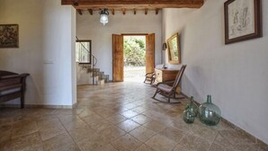 Une pièce spacieuse dotée d’un sol carrelé, de poutres en bois, d’un escalier, d’un bureau avec une chaise et d’une porte donnant sur l’extérieur.