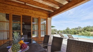 Une terrasse couverte avec une table dressée pour les repas, une piscine et une vue sur le paysage environnant.