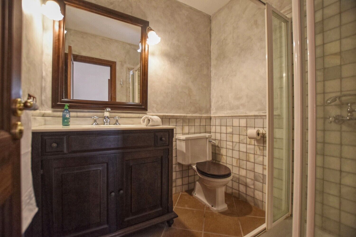 Ein Badezimmer mit einem dunklen Holz-Waschtisch, einer Toilette und einer Duschkabine aus Glas.