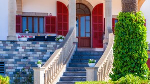 A staircase leading to a building entrance with red shutters, a stone balustrade, and potted plants. - Villa "Cas Siulet" with Sea View, 2 Private Terraces & Wi-Fi (Alcudia)