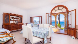 A dining area with a table set for four, a rocking chair, and a wooden cabinet with glass doors. - Villa "Cas Siulet" with Sea View, 2 Private Terraces & Wi-Fi (Alcudia)