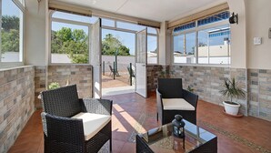 Un patio iluminado por el sol con mobiliario de mimbre, una mesa de vidrio y un ventilador de techo.