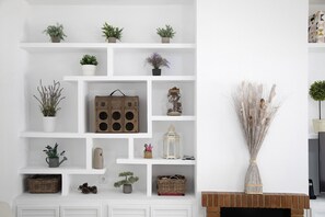 Un mur blanc orné de plusieurs étagères sur lesquelles sont disposés divers objets décoratifs, notamment des plantes, une lanterne et une valise ancienne.