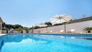 Piscina cristalina con sillas de descanso y sombrillas, rodeada por un muro bajo y vegetación.