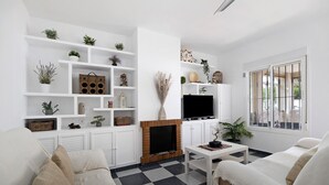 Una sala de estar con chimenea, sofás blancos, una mesa de centro y estantes con plantas y objetos decorativos.
