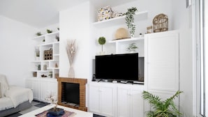 Una sala de estar con chimenea, televisor y varios objetos decorativos en estanterías.