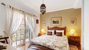 A bedroom with a large bed, a wooden headboard, two bedside tables with lamps, a window with curtains, and framed pictures on the wall. - Villa 'Little Paradise 25 Min From Lisbon' with Private Pool, Private Terrace and Wi-Fi (Azeitão)