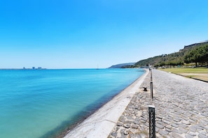 Una passeggiata costiera con un sentiero in pietra, acque blu cristalline e una città all'orizzonte.