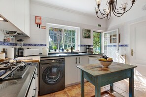 Een keuken met een wasmachine, een fornuis en een tafel met een schaal fruit.