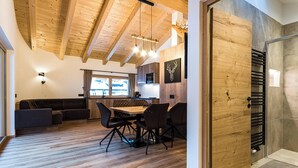 A modern interior with a wooden ceiling, a dining area with a table and chairs, a sofa, and a kitchen area with a stove. - Holiday Apartment "Piciulei Pitl" with Mountain View, Garden, and Wi-Fi (Selva di val gardena)