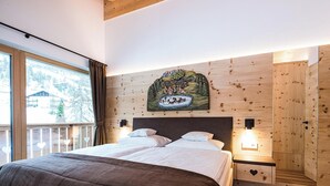 A bedroom with a bed, a headboard, a wall-mounted painting, and a window with curtains. - Holiday Apartment "Piciulei Pitl" with Mountain View, Garden, and Wi-Fi (Selva di val gardena)