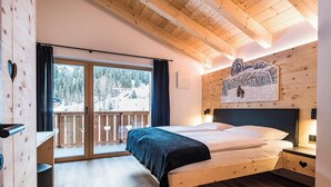 A wooden room with a bed, a window with curtains, a painting on the wall, and a balcony with a railing. - Holiday Apartment "Piciulei Pitl" with Mountain View, Garden, and Wi-Fi (Selva di val gardena)