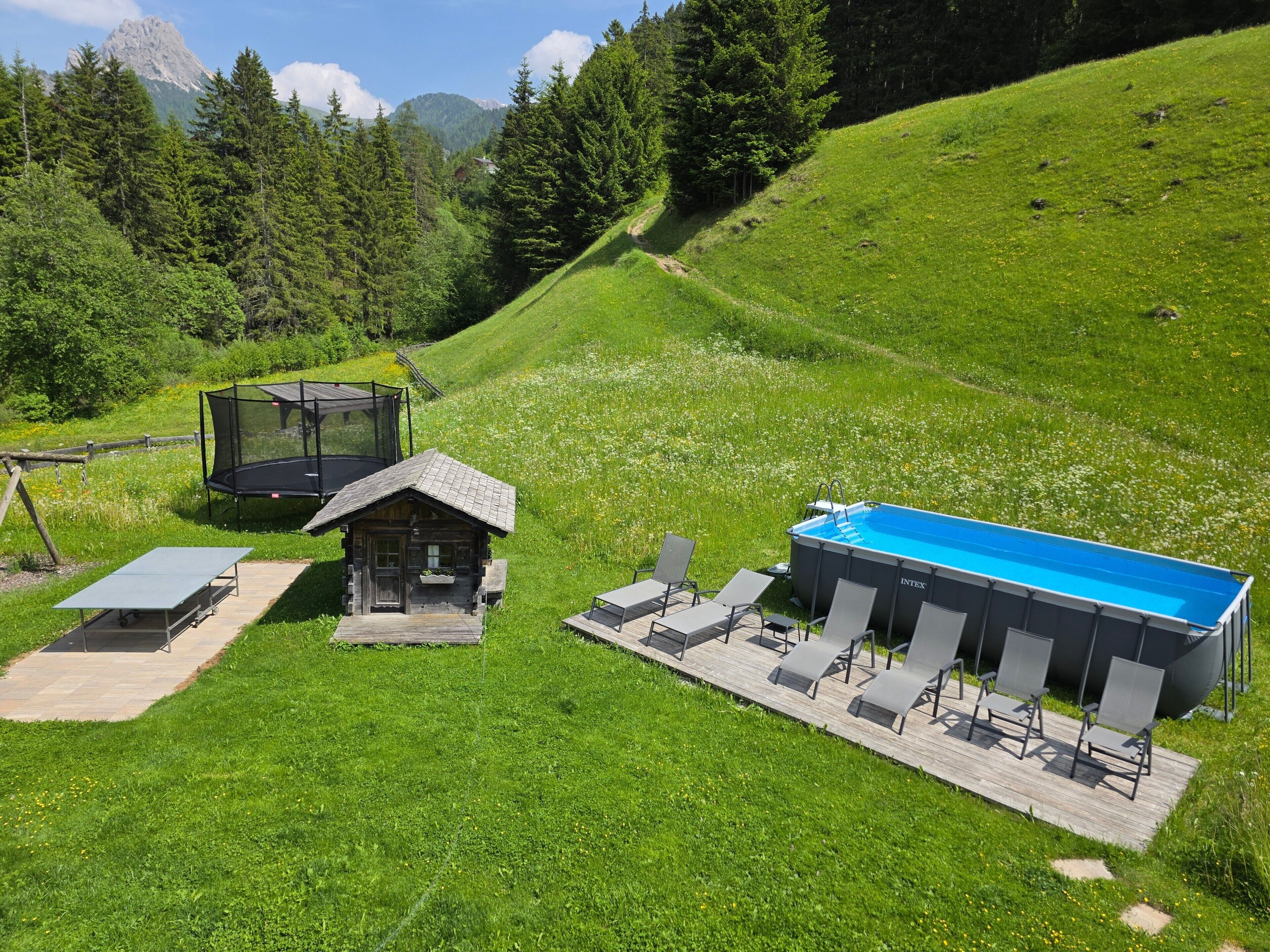 A mountain lodge with a trampoline, a small cabin, and a pool area.