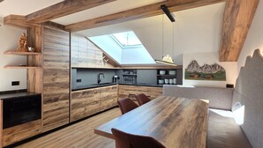A modern loft with exposed wooden beams, a skylight, a dining area with a wooden table and chairs, and a kitchen with wooden cabinetry. - Apartment "Piciulei Grant" with Mountain View, Garden, and Wi-Fi (Selva di val gardena)