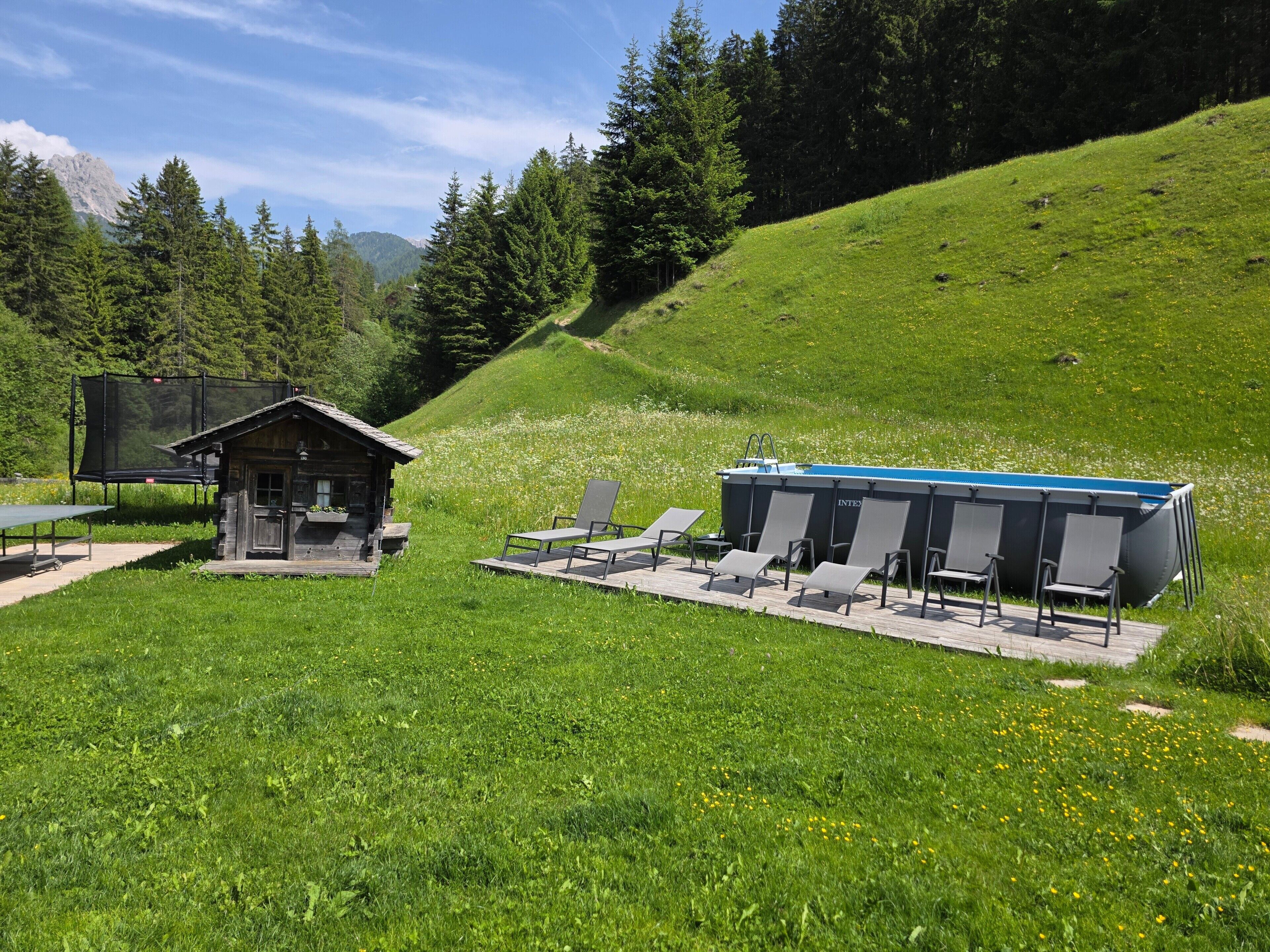 Une cabane dotée d’une petite terrasse, un espace piscine avec des chaises longues, et un paysage montagneux en toile de fond.