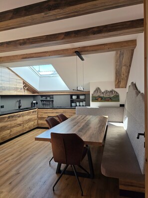 Una cocina moderna estilo loft con tragaluz, vigas de madera y un comedor con banco y sillas.