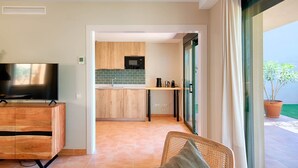 Una sala de estar moderna con televisor, un mueble de madera y vistas a la cocina y al balcón.