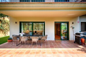 Un patio al aire libre con una mesa de comedor y sillas, una parrilla y vistas de la vegetación circundante.