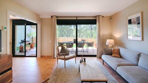 Una sala de estar con un sofá, una mesa de centro, una silla y vistas a un patio exterior con mesa y sillas.