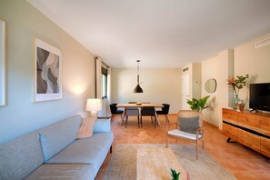 Un salon comprenant un canapé, une table à manger avec des chaises, un téléviseur, un meuble en bois et un miroir.
