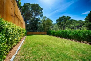 Une pelouse bien entretenue, avec une clôture en bois et une végétation arbustive dense.